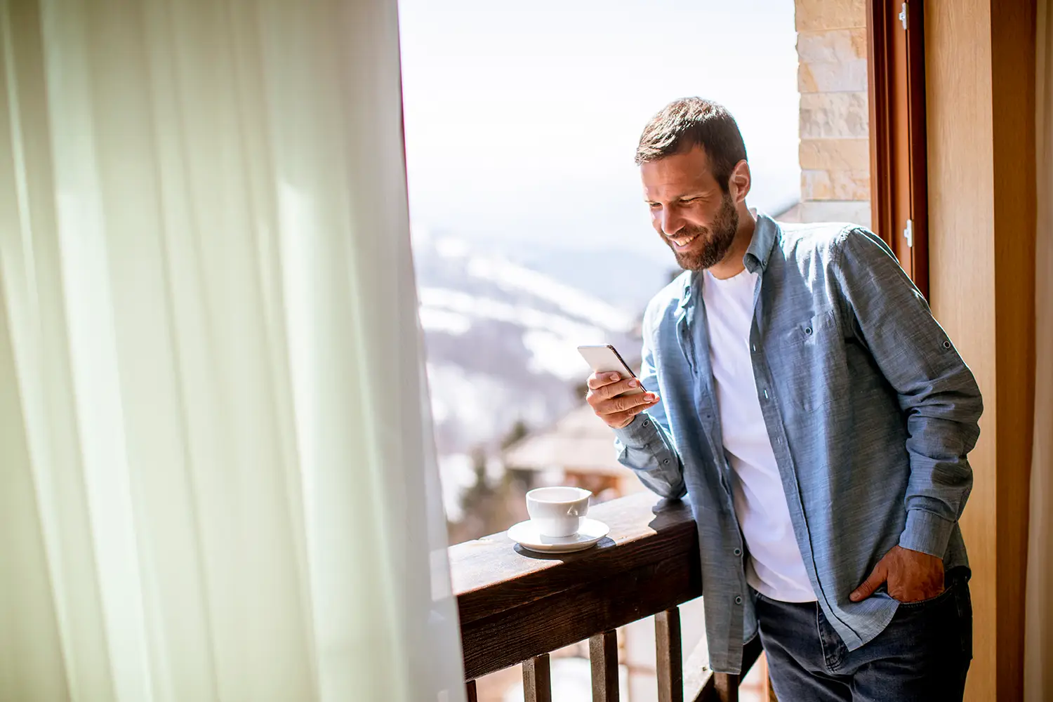 Gast am Handy mit einer Tasse Tee auf dem Balkon